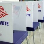 Photo of a series of voting booths with image of an American Flag and the word Vote on the side